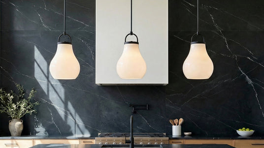 Three Naya pendant lights in black and opal glass hung in a modern kitchen with a dark stone backsplash