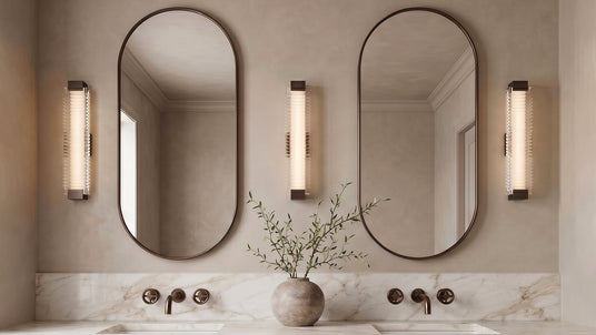 Three Enders LED Wall Sconces in Urban Bronze shown above a double vanity in an organic modern bathroom with stone countertops and plaster walls.