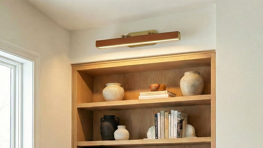 Jarrett LED Picture Light 32", Aged Brass and Cognac Vegan Leather shown above a built in bookcase.