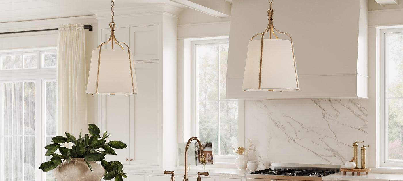 Two Isleton Small 14" wide Pendant lights, finished in Aged Gilded Brass with white fabric shades, hung in a bright white kitchen