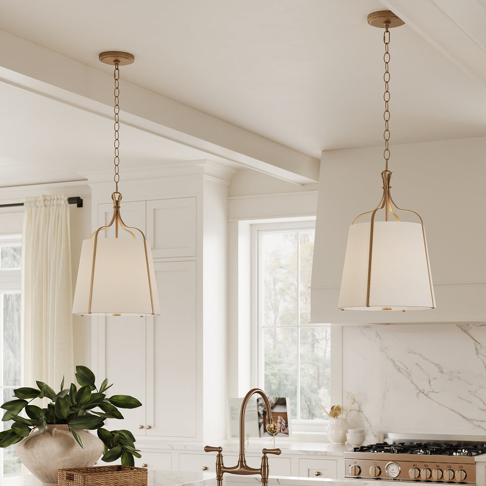 Two Isleton Small 14" wide Pendant lights, finished in Aged Gilded Brass with white fabric shades hung in a bright white kitchen