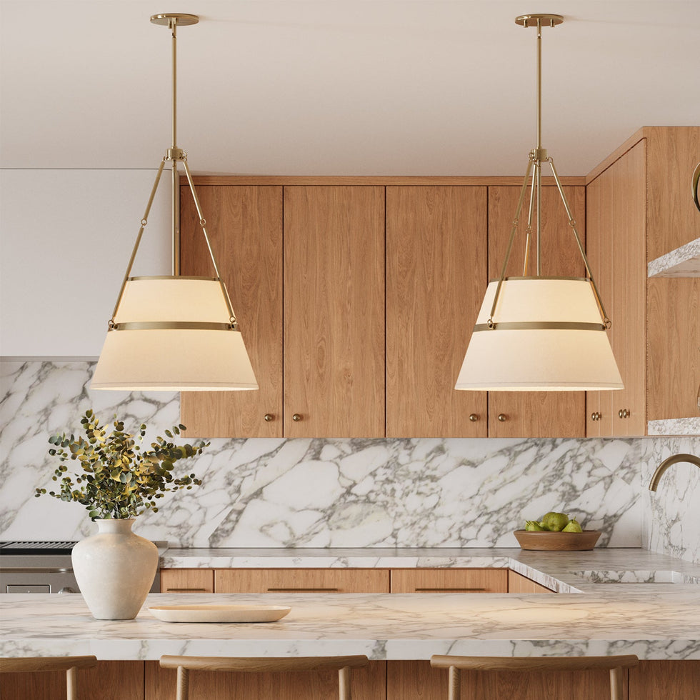 Two Julien Conical Pendant Lights in white and Aged Brass hung in a bright kitchen with white oaks cabinets and marble countertops.
