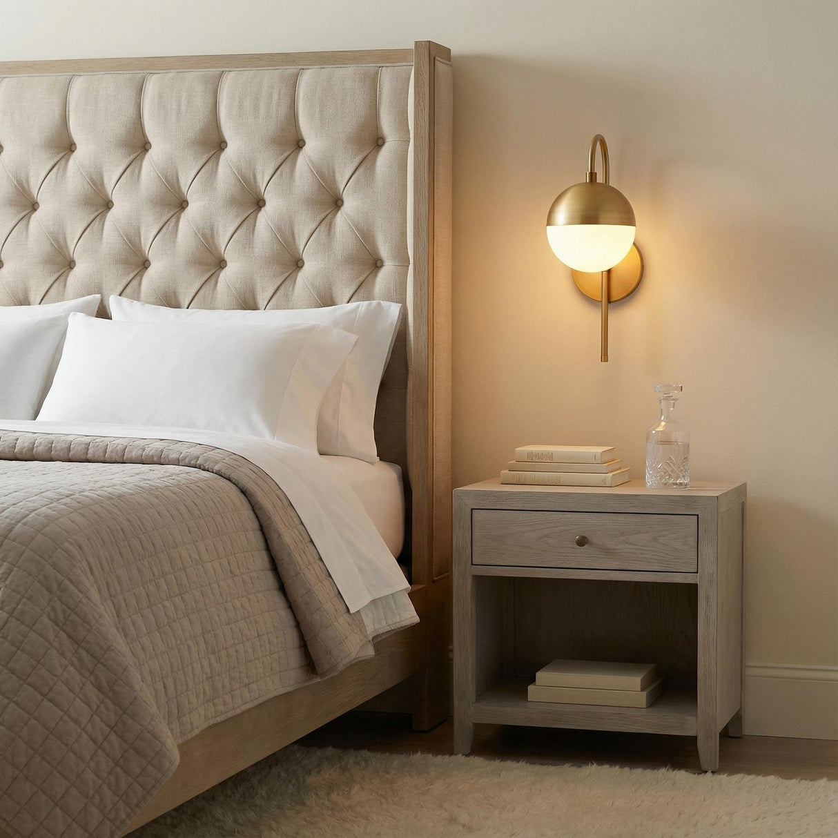 Powell Wall Sconce with Hooded White Globe, Aged Brass globe Wall Sconce in a Transitional Bedroom with tufted headboard.