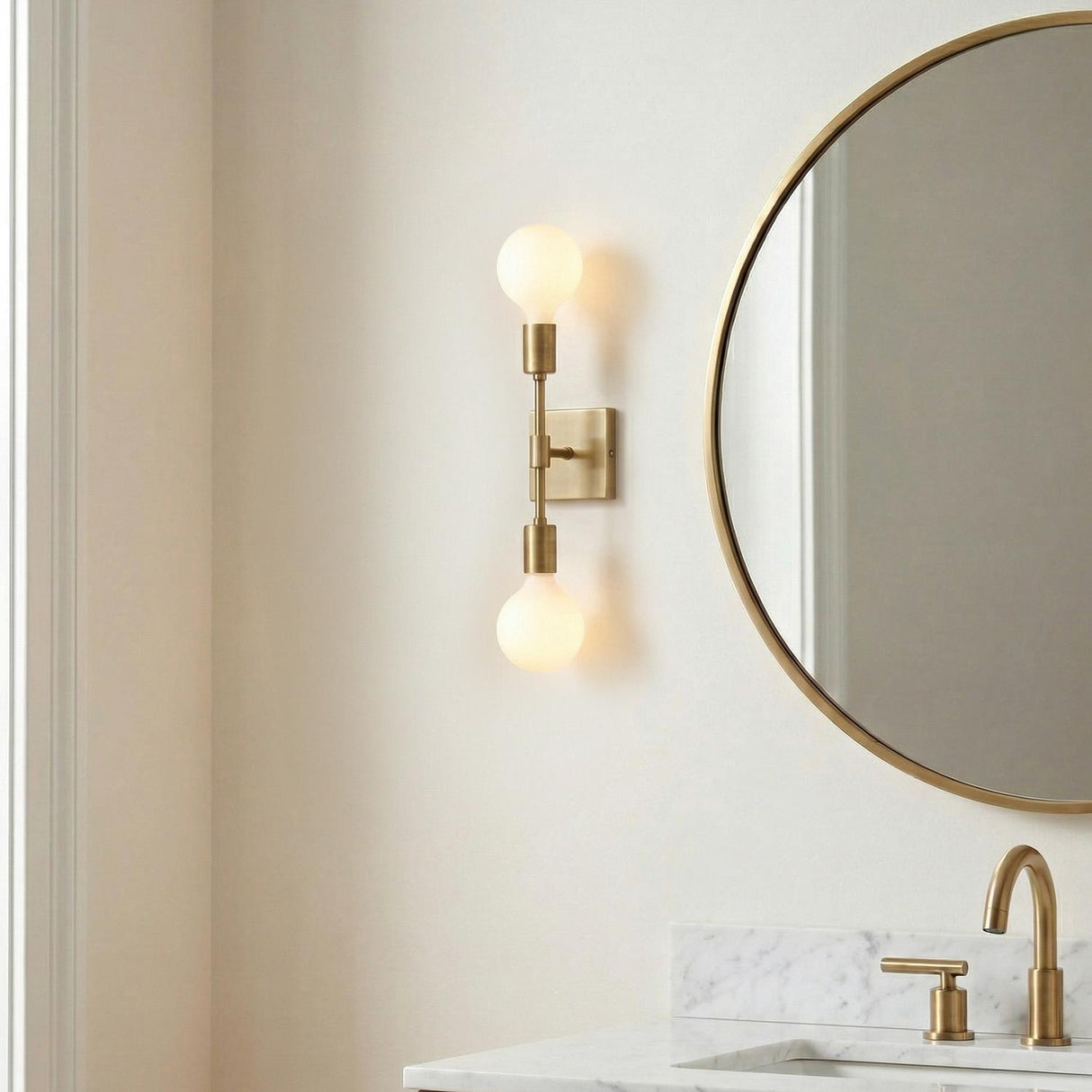 Prospect 2 Light Wall Sconce, Aged Brass globe Wall Sconce in a Modern Bathroom with a marble vanity and round mirror.