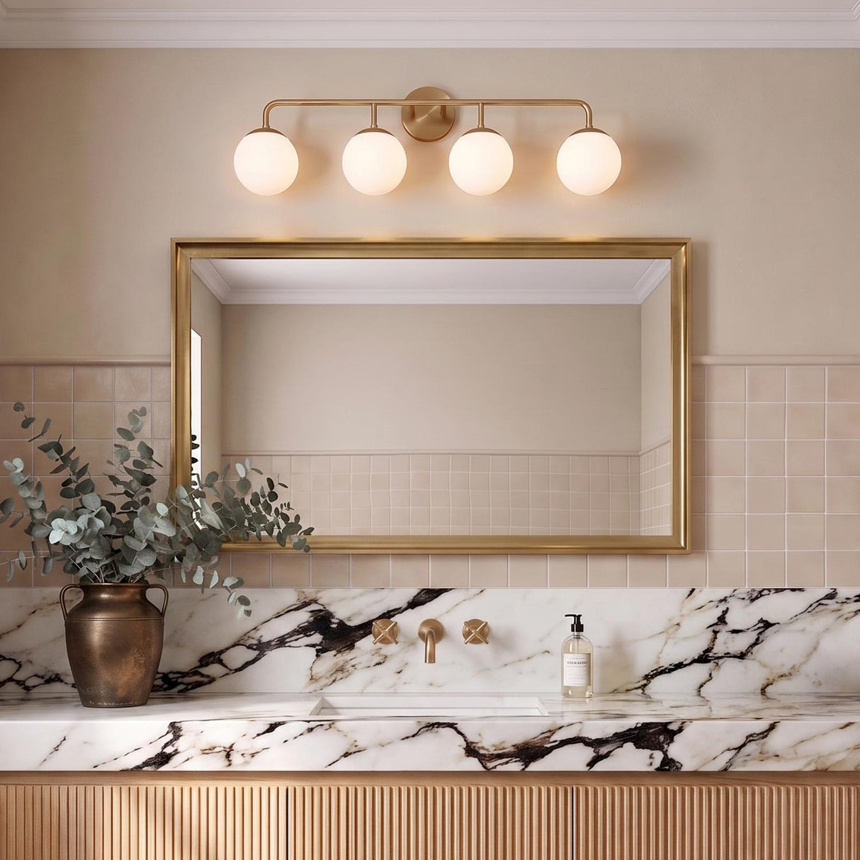 A transitional bathroom with a Castell 4 Globe Vanity in aged brass and frosted glass installed over a gold-framed mirror above a white marble countertop.