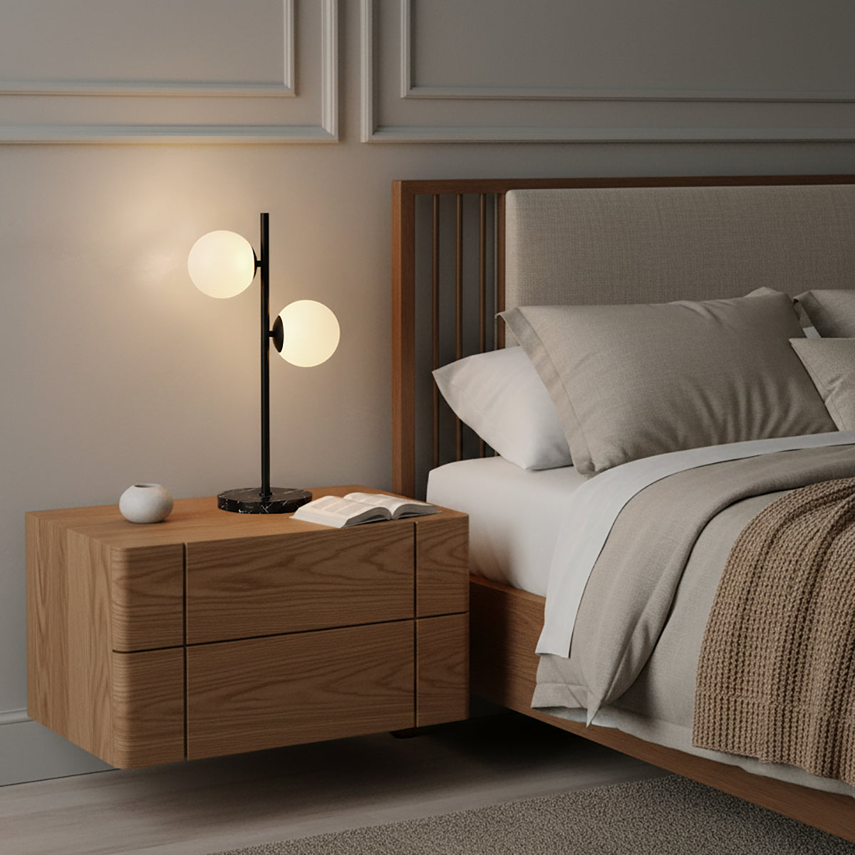Castell 2 Globe Table Lamp, Matte Black - A modern bedside table lamp with two frosted glass globes on a black stand, resting on a wooden nightstand next to a bed.