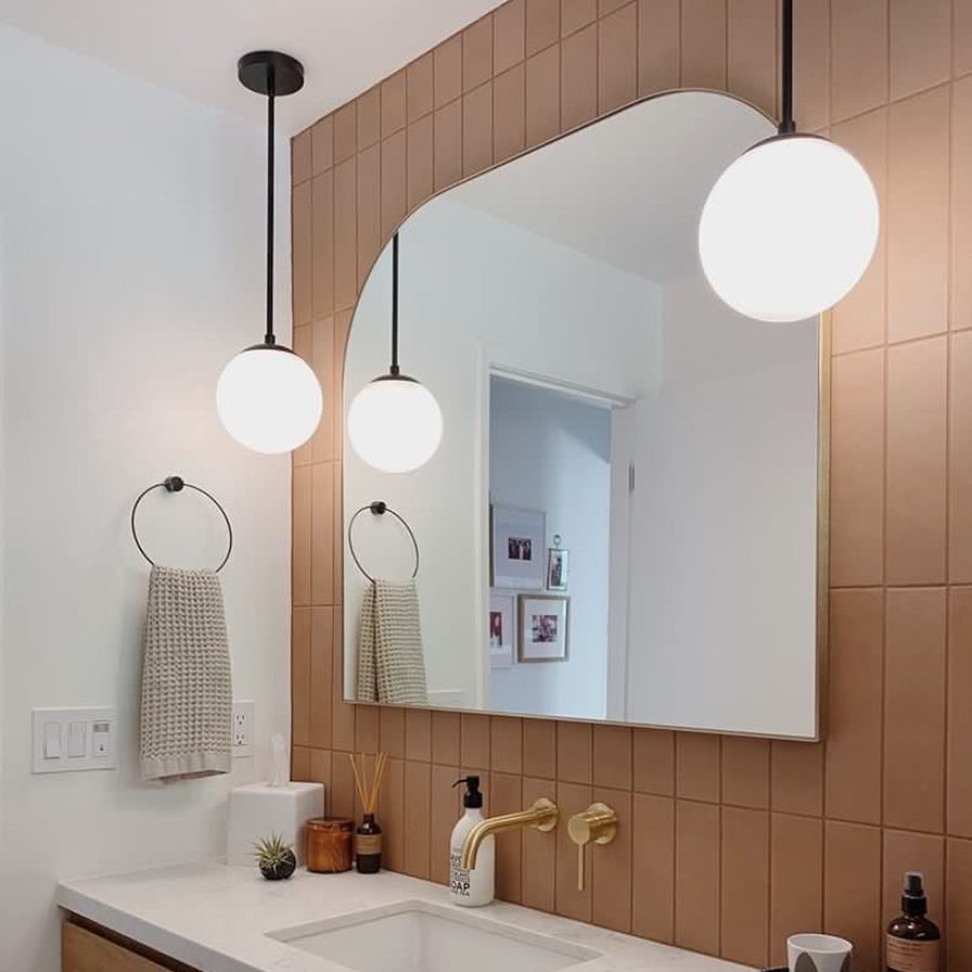 Customer photo of two Castell LED 8" Globe Pendant Lights, Opal White Glass and Matte Black metal finish, hanging in a modern bathroom as vanity lights