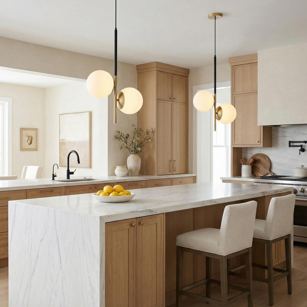 A modern kitchen features two Castell 2 Globe Pendant 15.5", Matte Black and Aged Brass fixtures over a white marble waterfall island with light wood cabinets.