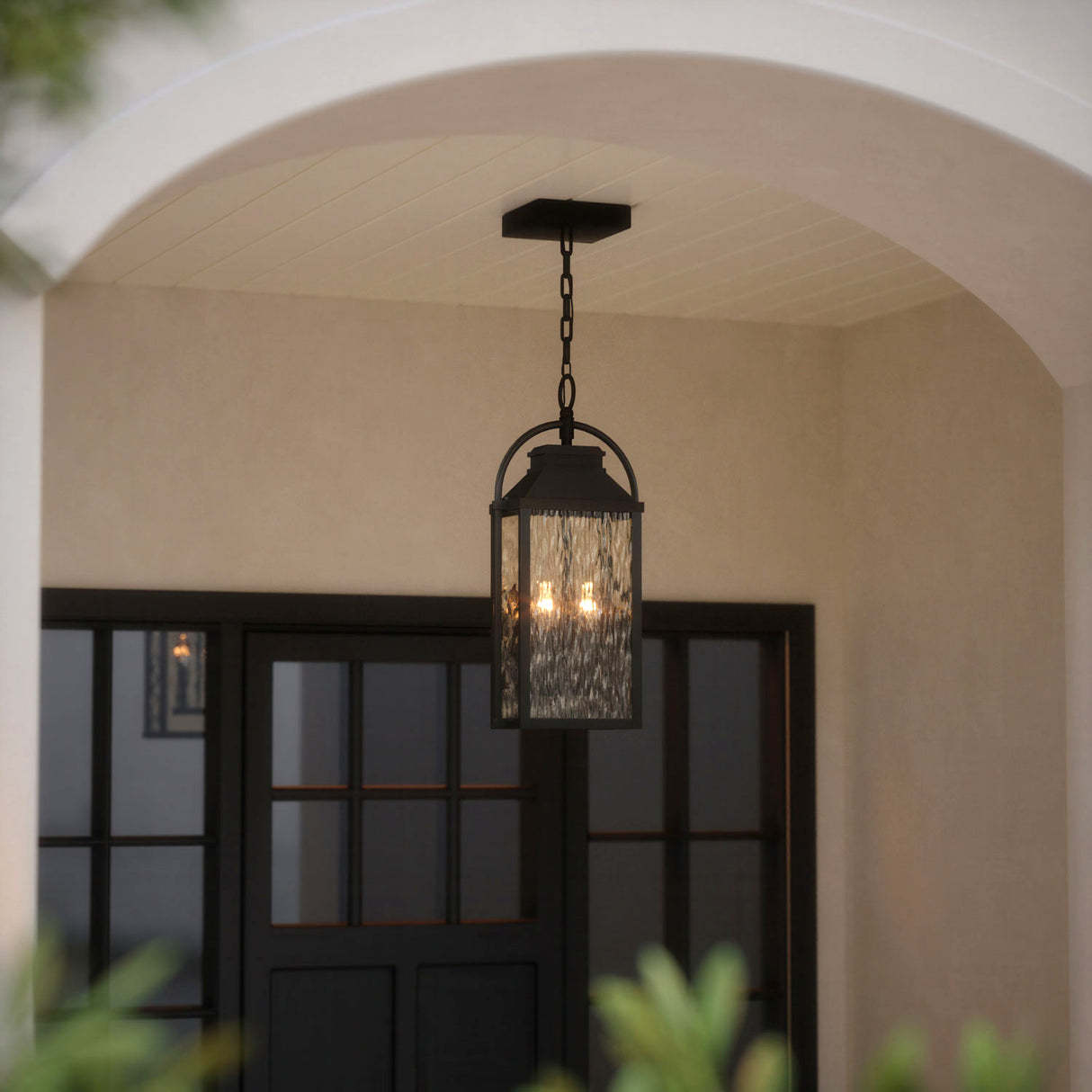Preston outdoor hanging light with clear water glass and textured black finish is shown under a porch with an arched entryway.