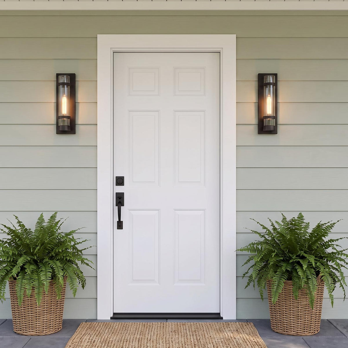 A modern farmhouse entry featuring light green siding and two Glenn Outdoor Wall Light, Matte Black fixtures glowing while flanking a white front door above potted ferns.