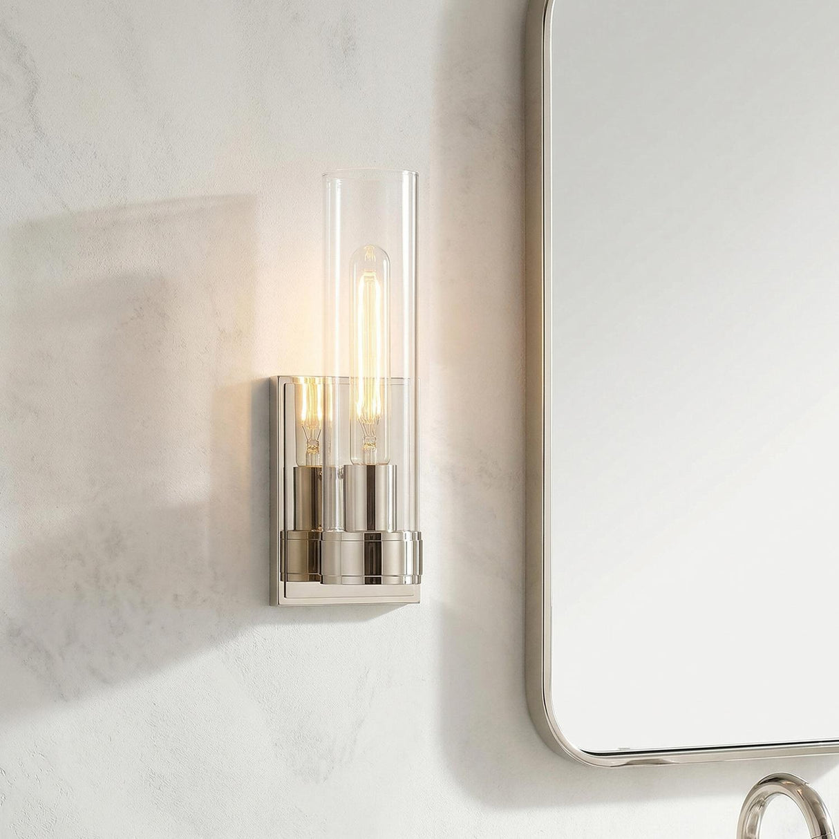 Sutton 1 Light Wall Sconce, Polished Nickel linear Wall Sconce in a Contemporary Bathroom with a white marble wall and silver mirror.