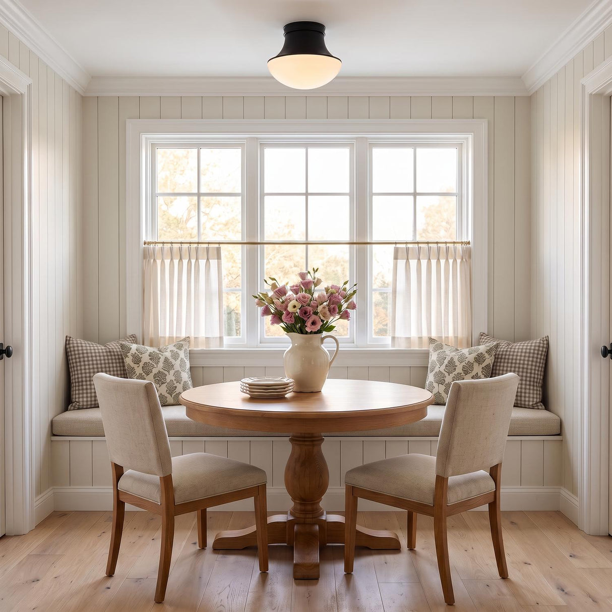 A cottage dining nook with the Jayden Flush Mount 14", Matte Black on the ceiling over a round wood pedestal table and built-in window seat with shiplap walls.