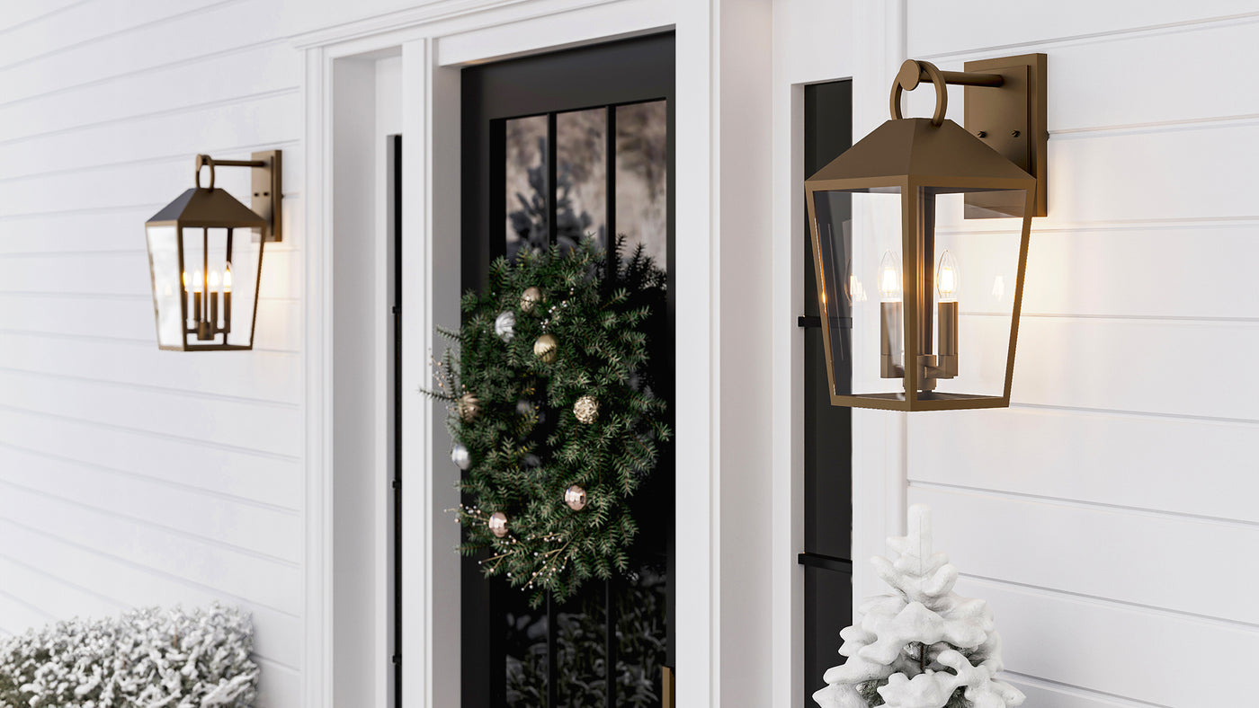 Two Outdoor Burnished Brass Lantern Wall Lights, the Cole Collection, on a wintery porch with white cladding and a wreath on the door