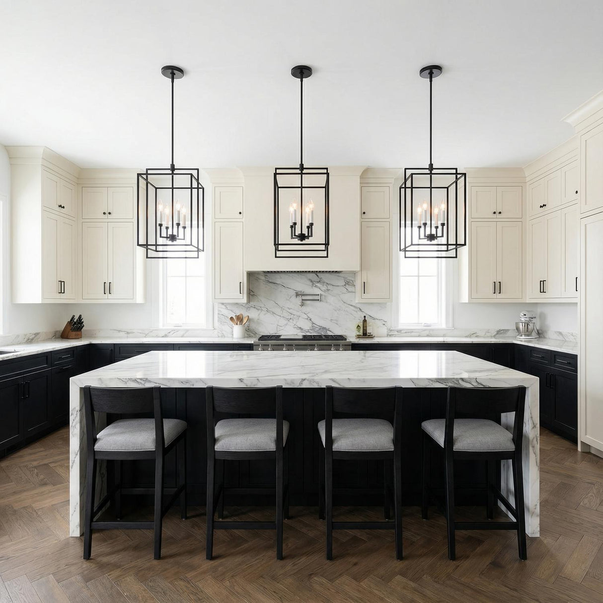 A transitional kitchen features three Noa 4 Light Pendant 13 inch matte black lantern pendants over a white marble waterfall island with a matching stone backsplash.