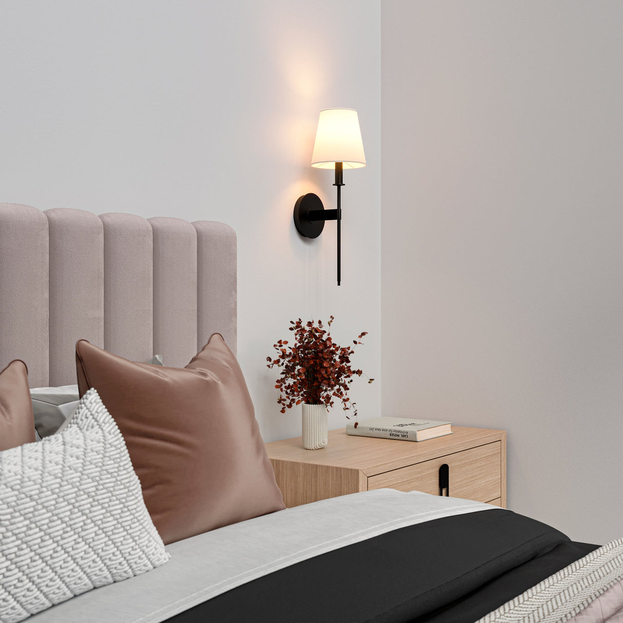 Taylor 19" tall wall sconce in matte black with a white fabric shade shown as a bedside light in a modern bedroom with dusty rose colored bedding.