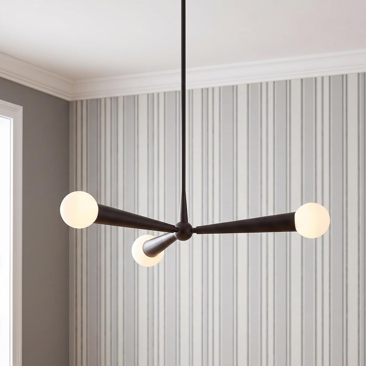 A mid-century dining room featuring a matte black Nova 3 Light Pendant with frosted glass globes suspended from a standard ceiling against gray and white striped wallpaper.