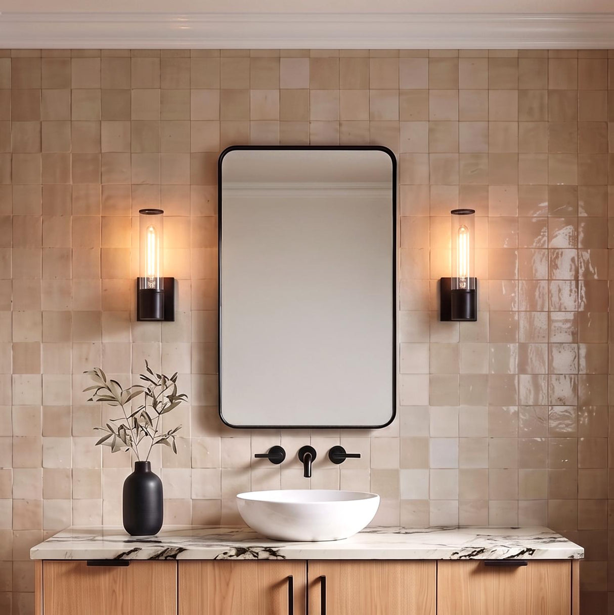 A modern bathroom with two matte black Lea Wall Sconces with clear glass cylinders flanking a rectangular mirror over a marble countertop and tan zellige tile.