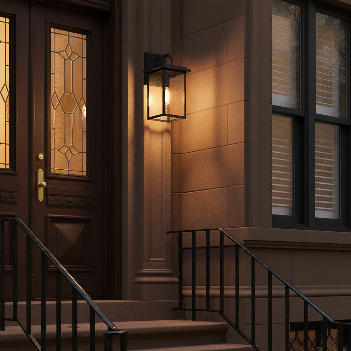 Paterson Outdoor Wall Light, Large - A black outdoor wall light with a clear seeded glass lantern illuminates a dark brown doorway with a decorative glass pane.