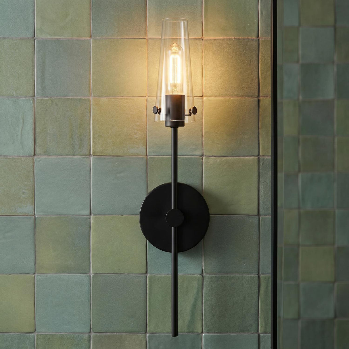 A modern bathroom with a matte black Mason 1 Light Wall Sconce featuring a tapered clear glass shade mounted on a green zellige square tile wall.