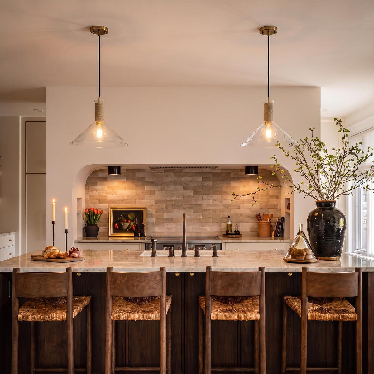 A modern farmhouse kitchen with two Nora Glass Pendants 16" featuring jute rope accents and brass hardware suspended over a marble island with walnut woven barstools.