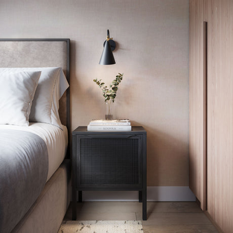 Faye conical metal wall sconce in black with brass accents shown as a bedside light in a modern bedroom with neutral colors and a black wood bedside table.