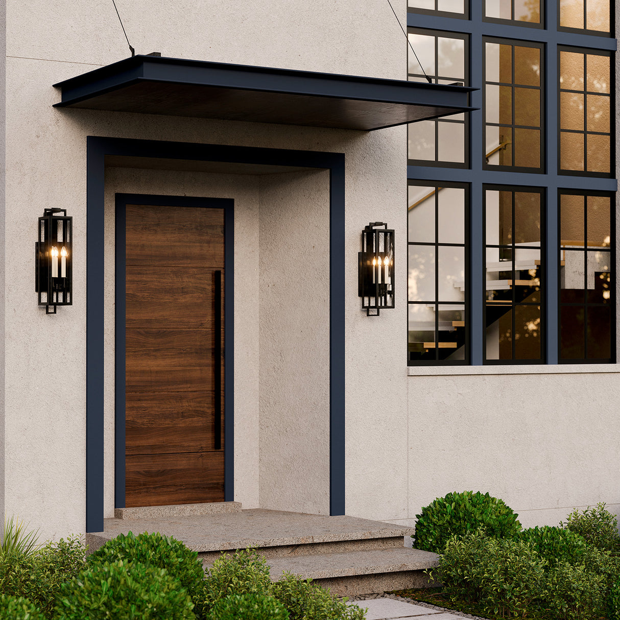 Two Everett outdoor medium wall lights in black with cream candle sleeves and clear glass are shown flanking an entry to a large modern home.