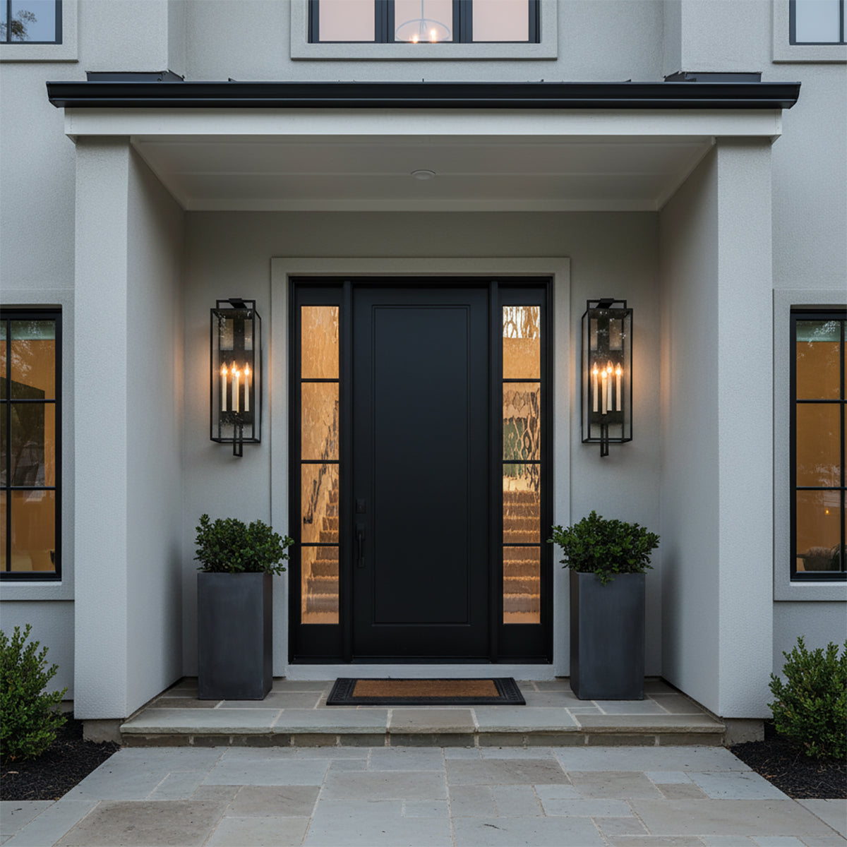 Everett Outdoor Wall Light, Large, Forged Iron Black - Two black lanterns with candle-style lights flank a black front door on a home's exterior.