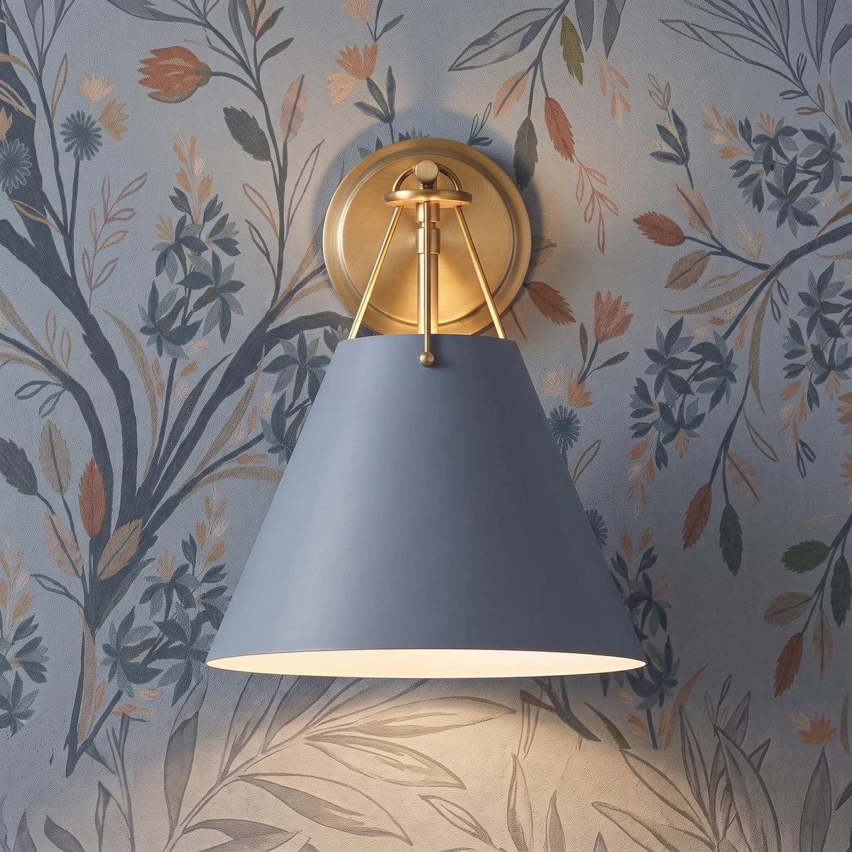 A transitional foyer features the Bowie Wall Sconce, French Blue and Brass with a brushed brass backplate mounted against botanical floral wallpaper.