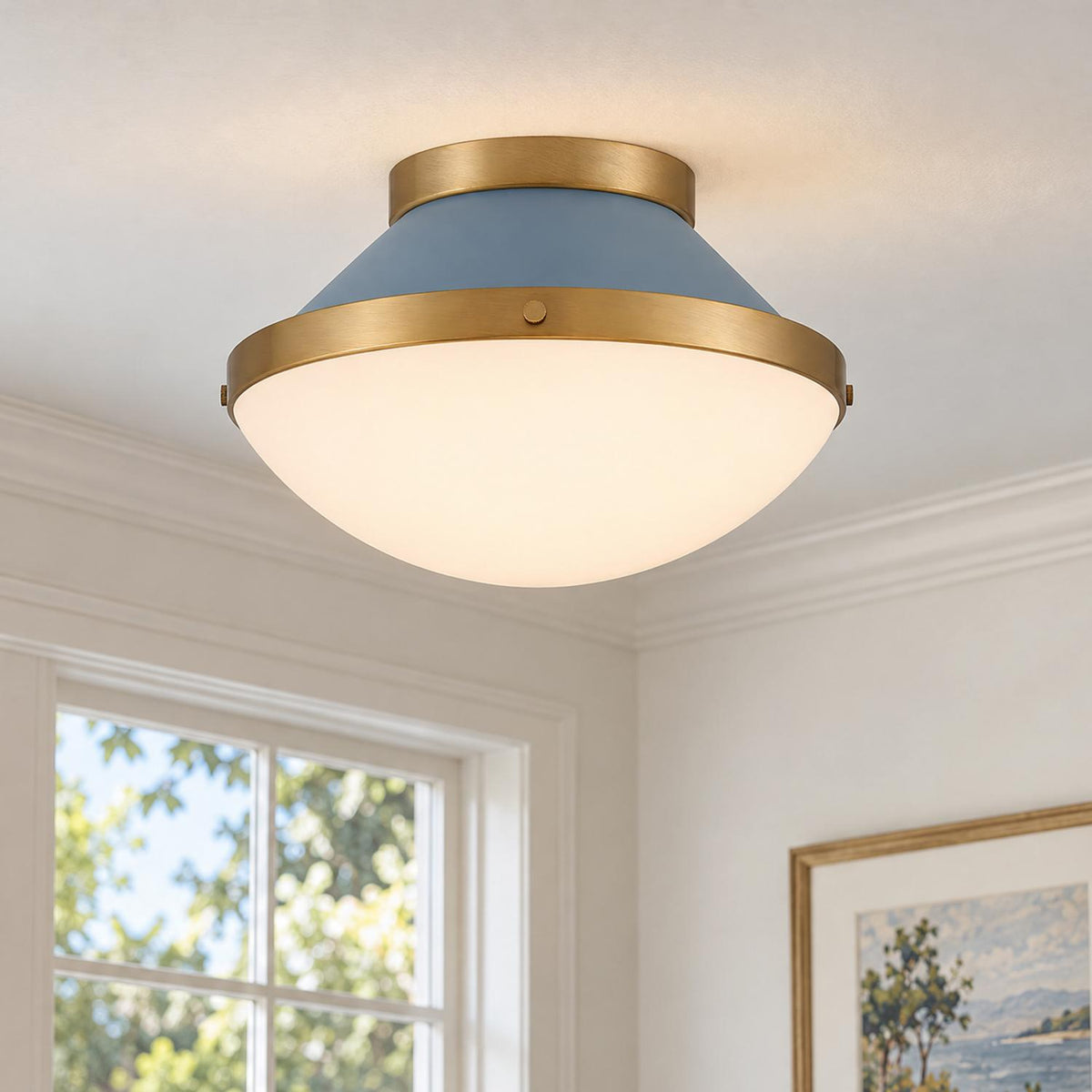A transitional living room features the Blair Flush Mount 12", French Blue and Brass fixture illuminated on a white ceiling beside crown molding and framed art.