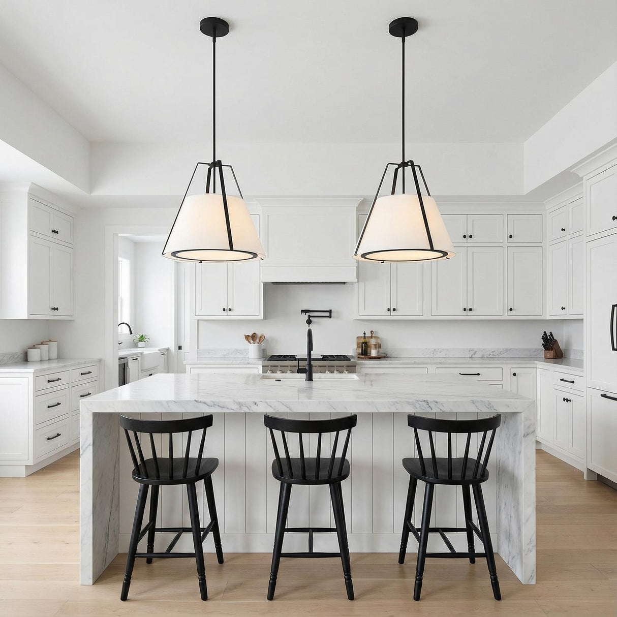 A modern kitchen featuring two Hoyt Pendant 20", Black with matte black frames and white linen shades hanging over a white marble waterfall island.