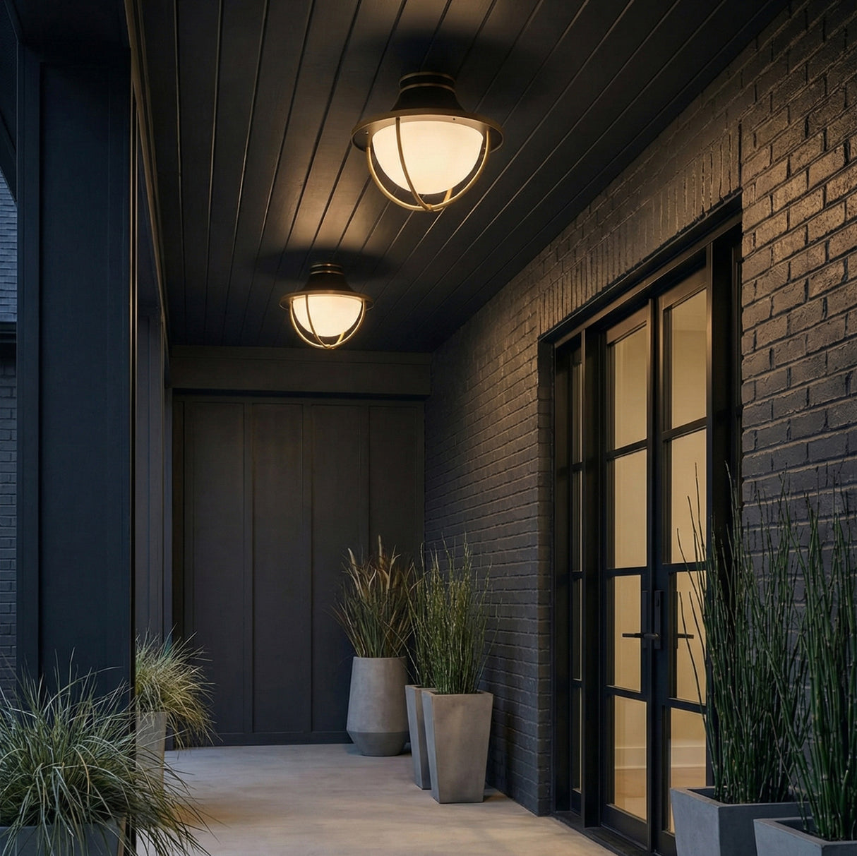 Tobin Outdoor Flush Mount, Black and Brass geometric globe flush mount in a Modern Outdoor with a dark brick wall and concrete planters.