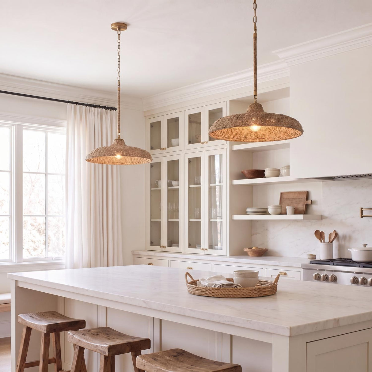 A coastal kitchen with two Sarina Pendants in lake grass and soft brass over a white marble island with wood stools and white shaker cabinets.