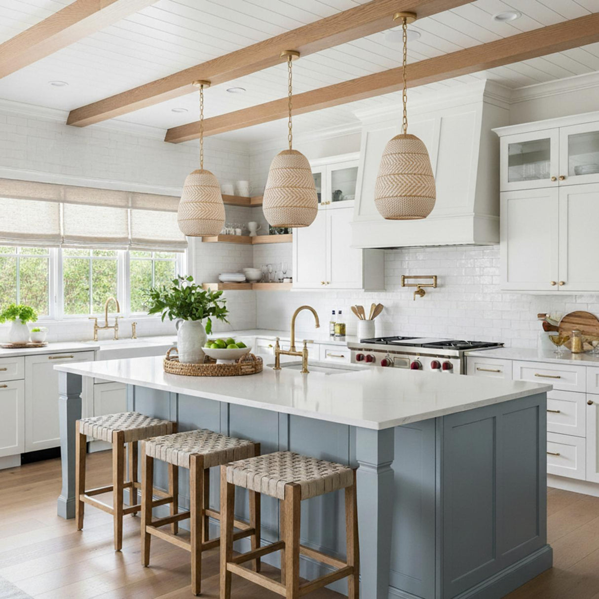 A coastal kitchen featuring three Sienna 3 Light Pendant 16", Rattan and Soft Brass fixtures suspended over a blue island with white counters under a beamed shiplap ceiling.