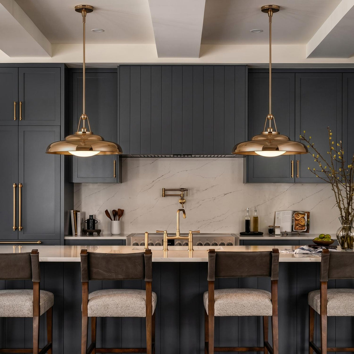 A transitional kitchen with two Neville Pendant 20-inch saucer pendants in polished brass over a white quartz island featuring dark gray cabinetry under a white beamed ceiling.