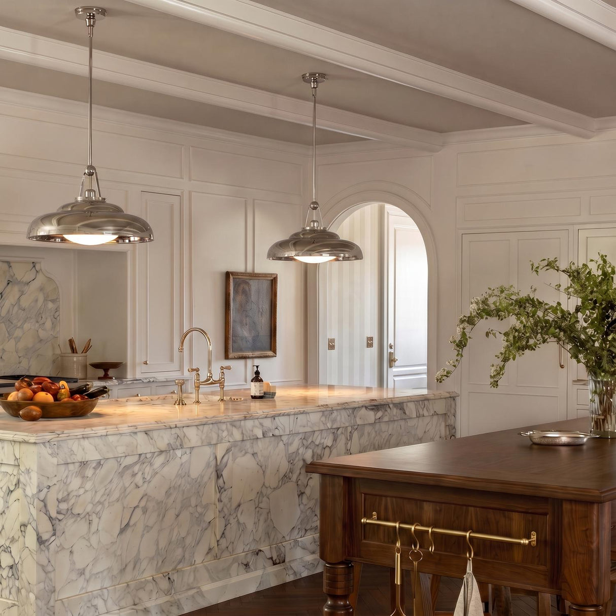 A traditional kitchen featuring two Neville Pendant 20", Polished Nickel fixtures over a heavily veined marble island and a walnut table under a beamed ceiling.