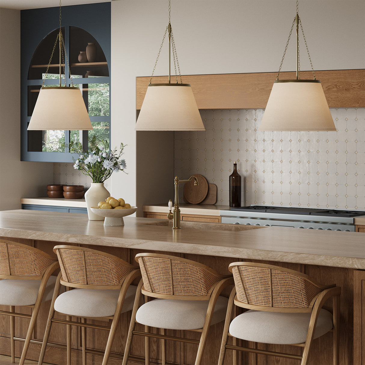 Modern kitchen with three Adrian 18" Pendant lights in Antique Brass, hung above a stone island, with wicker chairs.