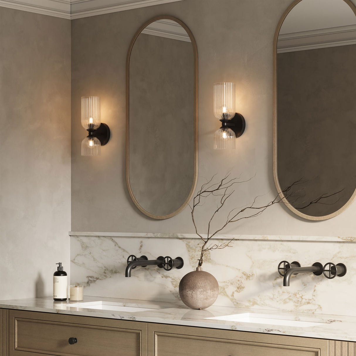 Elle Sconce in clear glass with Matte Black finish is shown in a bathroom with oval shaped mirrors and wooden details
