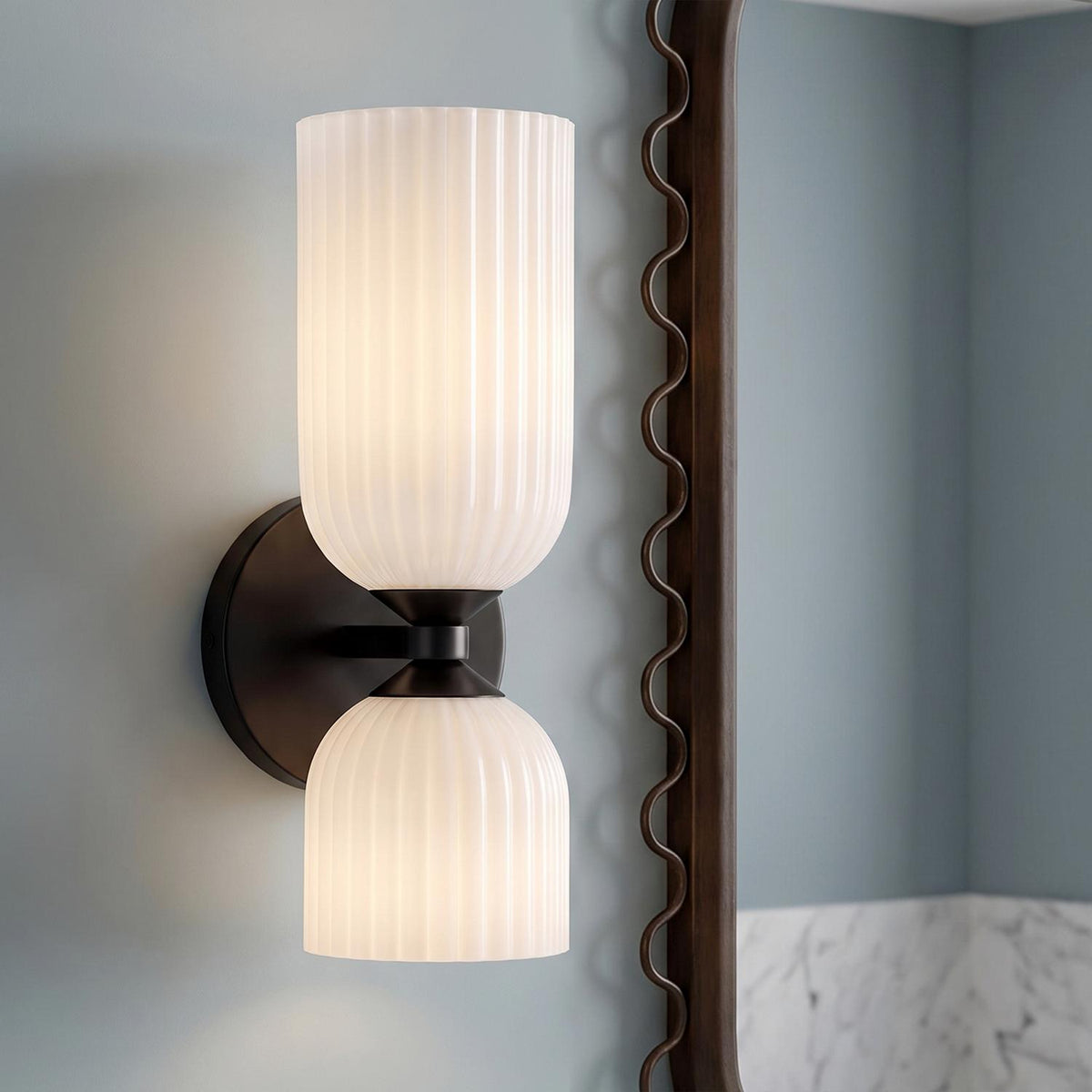 A modern bathroom features the Elle Wall Sconce, Matte Black and Milk Glass, mounted next to a decorative mirror above a marble backsplash.