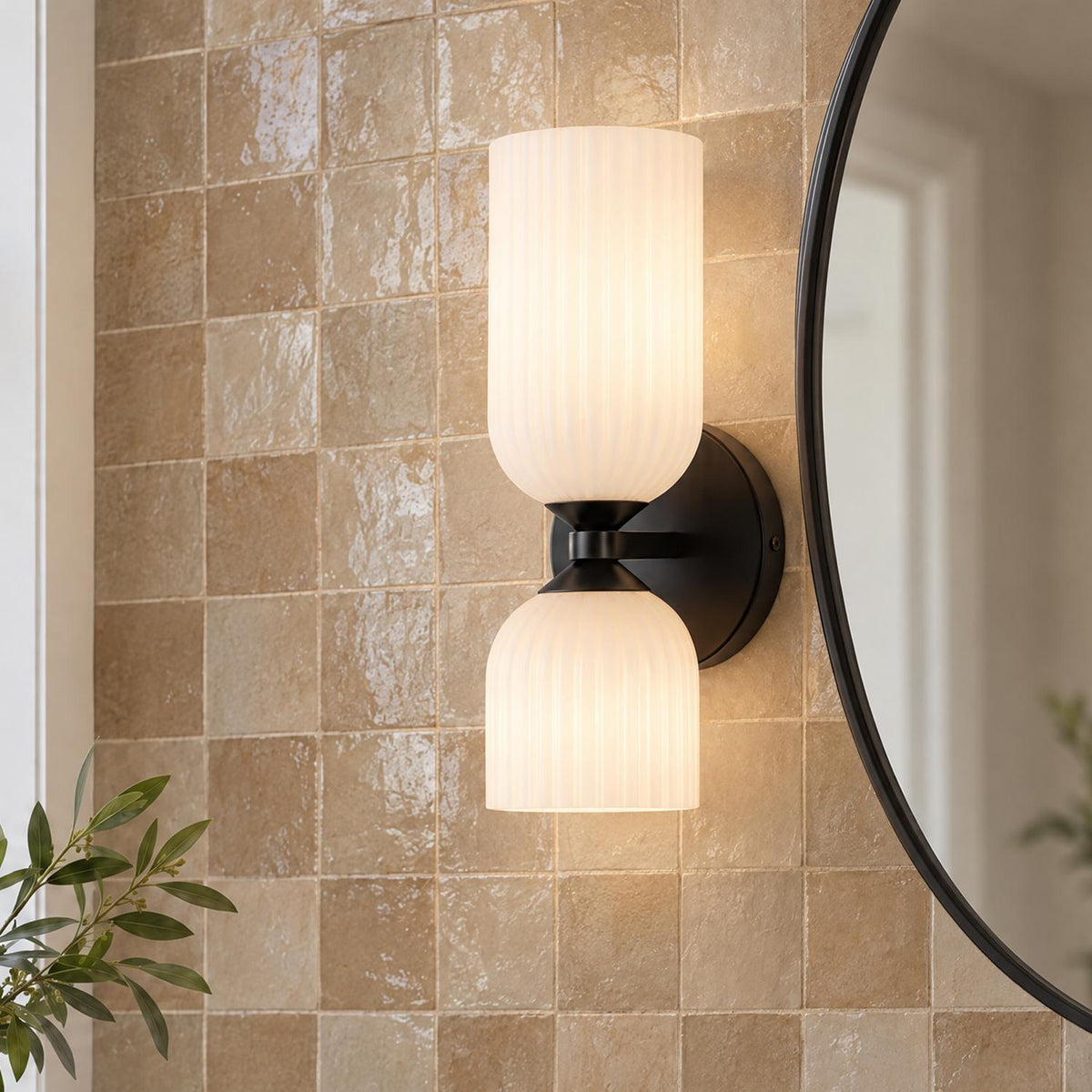 A transitional bathroom features the Elle Wall Sconce, Matte Black and Milk Glass mounted beside a round black mirror on a beige glazed zellige tile wall.