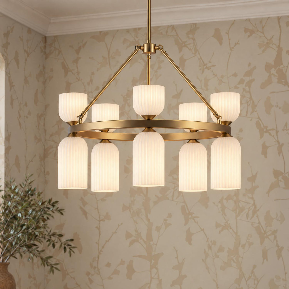 A transitional dining room features the Elle Chandelier 26", Brushed Brass and Milk Glass with ribbed shades hanging before warm botanical wallpaper and a potted plant.