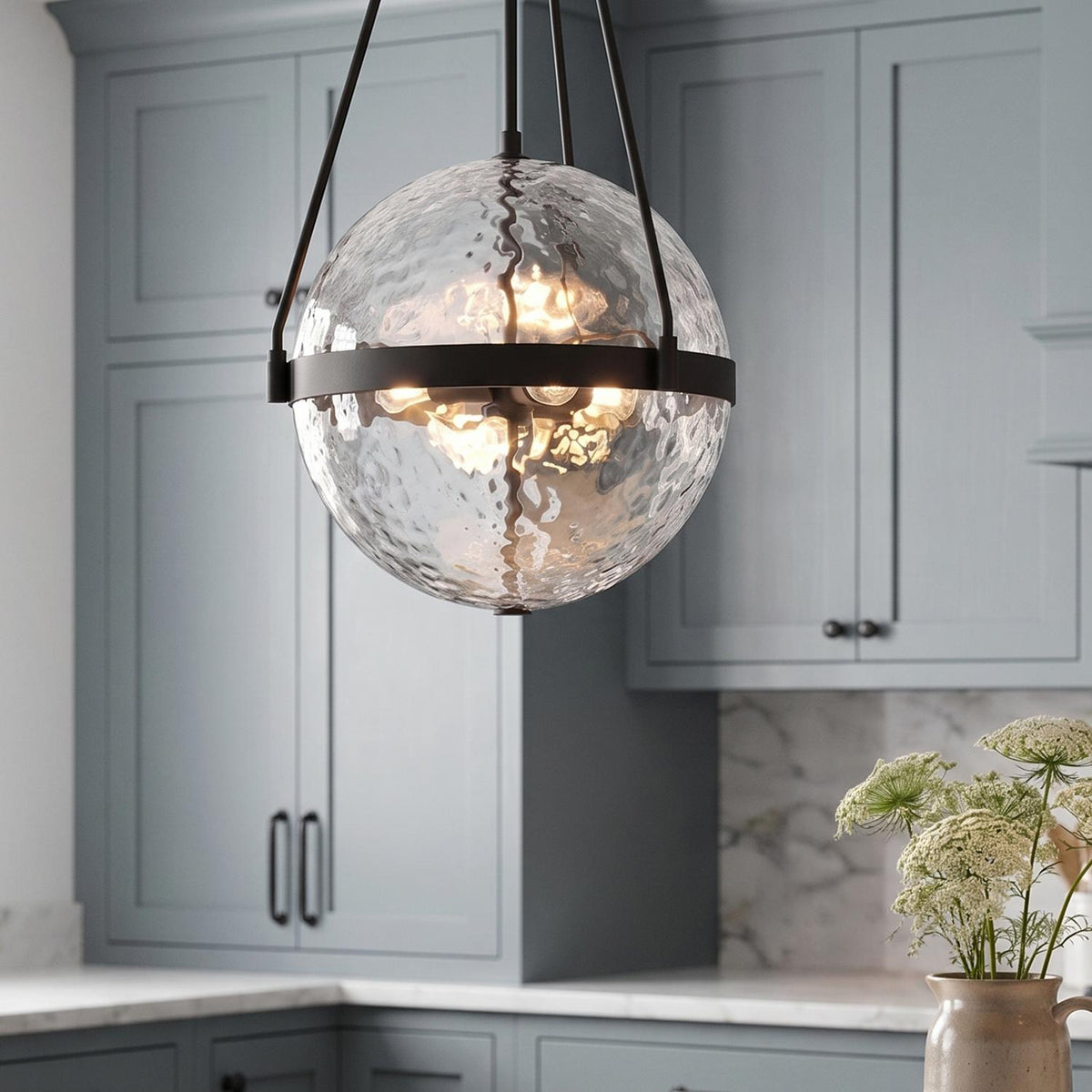 A transitional kitchen with a Darcy Large Pendant 18", Matte Black and Water Glass suspended over a white marble countertop and blue-gray shaker cabinets.