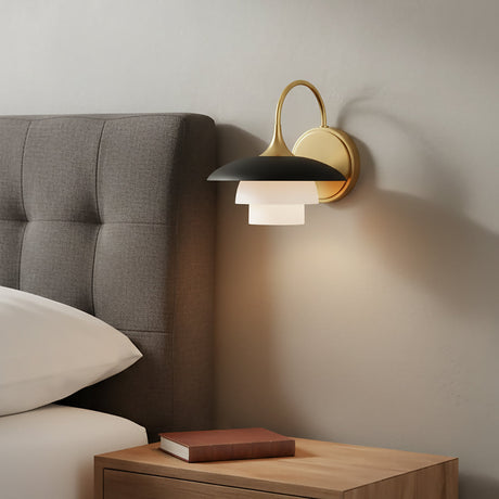 Wall-mounted Wren Wall Sconce above a nightstand next to a bed with grey fabric tufted headboard.
