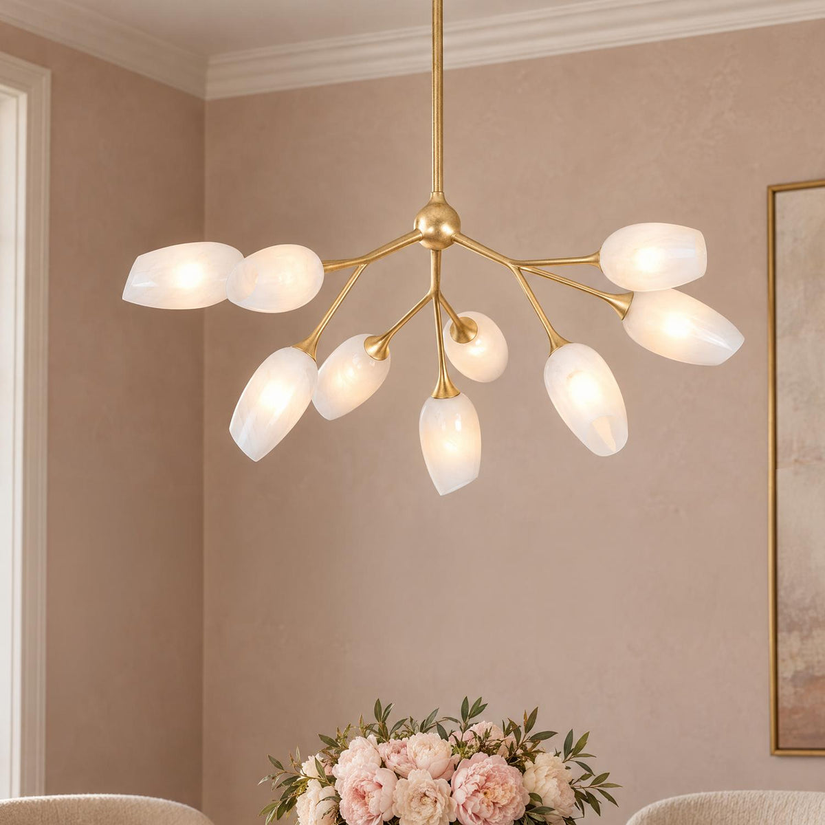 A contemporary dining room featuring the Amara 9 Light Chandelier with gold leaf finish hanging over a pink peony floral centerpiece on a dining table.