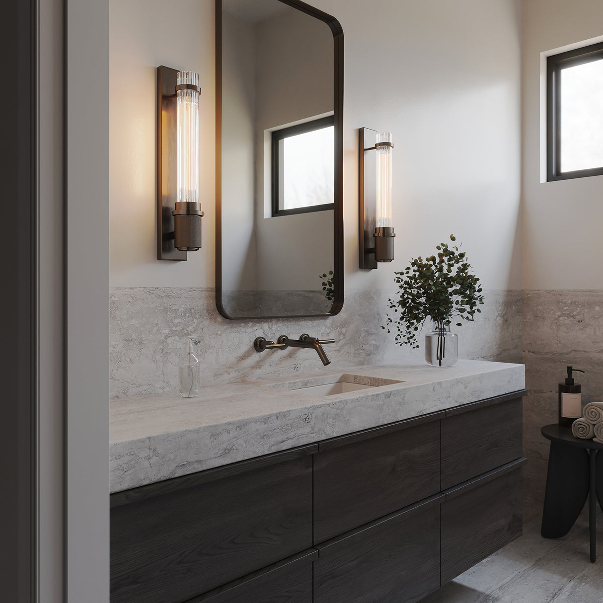 Zeke Wall Sconce 16", in Old Bronze finish and fluted glass, show in in a modern bathroom with slab countertops and dark accents.