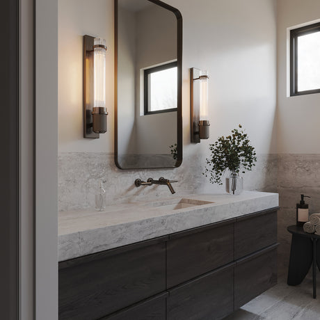 Zeke Wall Sconce 16", in Old Bronze finish and fluted glass, show in in a modern bathroom with slab countertops and dark accents.