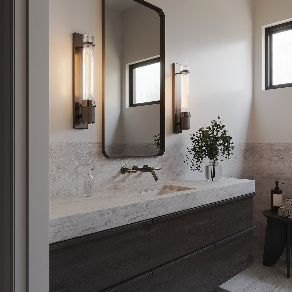 Zeke Wall Sconce 16", in Old Bronze finish and fluted glass, show in in a modern bathroom with slab countertops and dark accents.