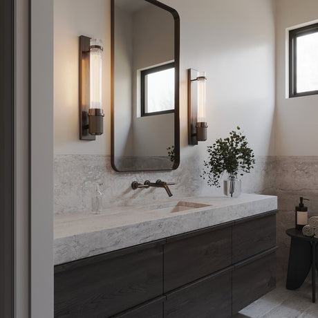 Zeke Wall Sconce 16", in Old Bronze finish and fluted glass, show in in a modern bathroom with slab countertops and dark accents.