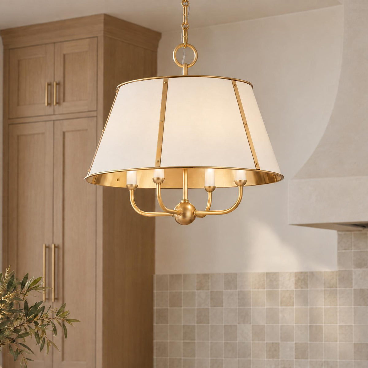 A transitional kitchen displays an aged brass pendant light with an off-white tapered shade hanging near light wood cabinets and a square tiled backsplash.
