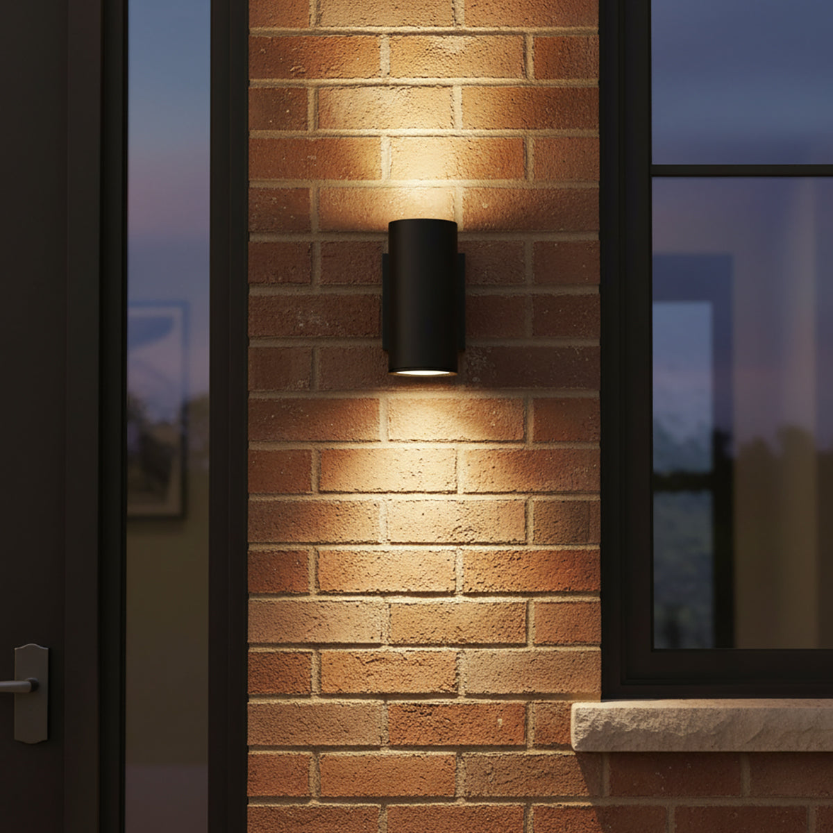 Beck Outdoor Cylinder Wall Light, 9" tall in Black finish, shown at dusk on a brick wall, with up and down lights.