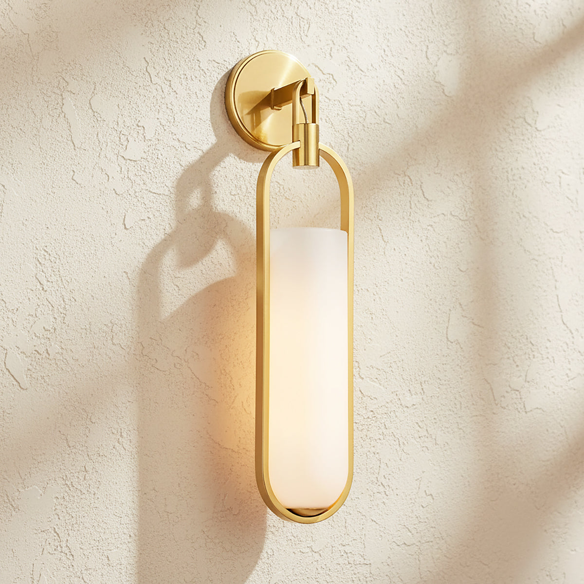 Micah LED Wall Sconce 22", Aged Brass - A gold sconce with a white shade on a textured wall.